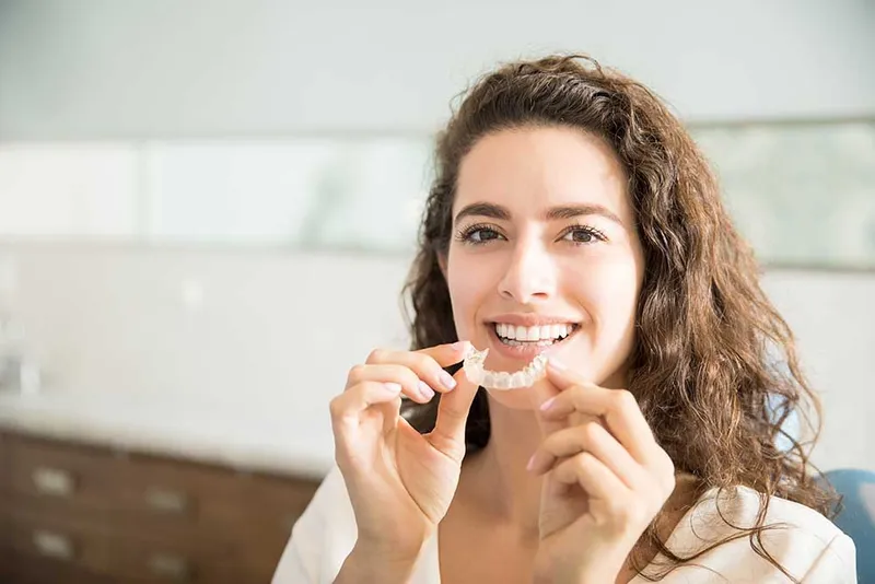 A close up of a woman smiling and holding her invisalign braces